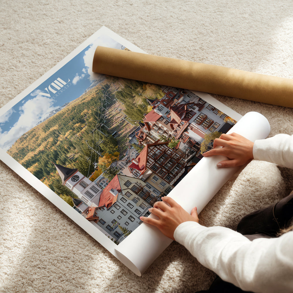 Person unrolling a Colorado travel poster of Vail ski town, showcasing autumn foliage and mountain scenery.